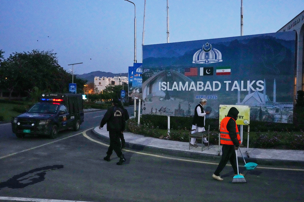 A worker cleans the street as police officers walks towards their vehicle outside a media center close to Serena Hotel, the venue for the U.S. Iran officials meeting, in Islamabad, Pakistan, Sunday, April 12, 2026. (AP Photo/Anjum Naveed)