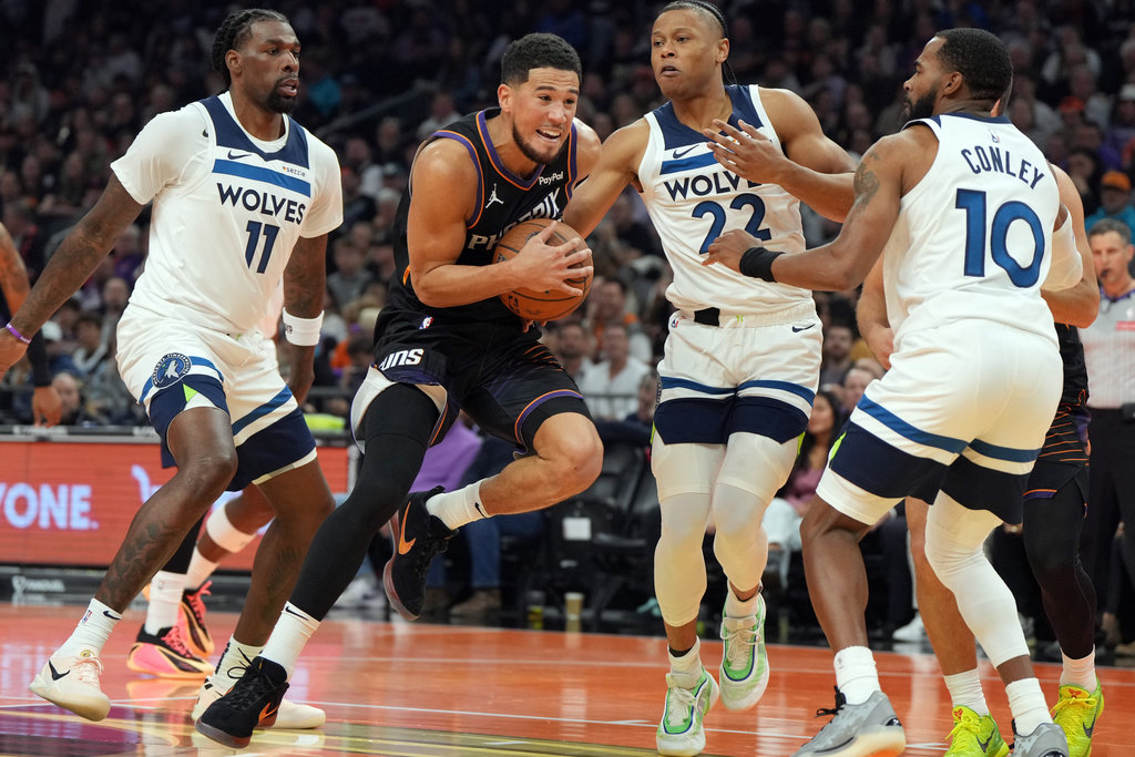 Phoenix Suns guard Devin Booker, second from left, drives between Minnesota Timberwolves center Naz Reid (11), guard Jaylen Clark (22) and guard Mike Conley during the first half of an NBA Cup basketball game, Friday, Nov. 21, 2025, in Phoenix. (AP Photo/Rick Scuteri)