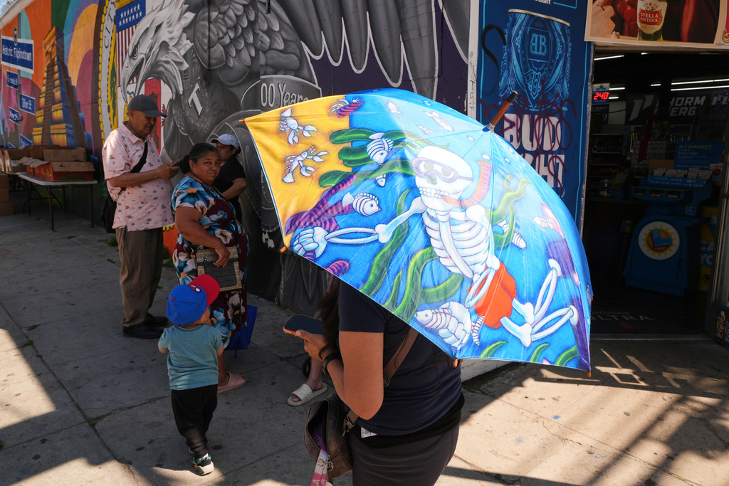 People cover themselves from the heat with umbrellas while waiting to receive food items at a donation site Wednesday, March 11, 2026, in Los Angeles. (AP Photo/Damian Dovarganes)