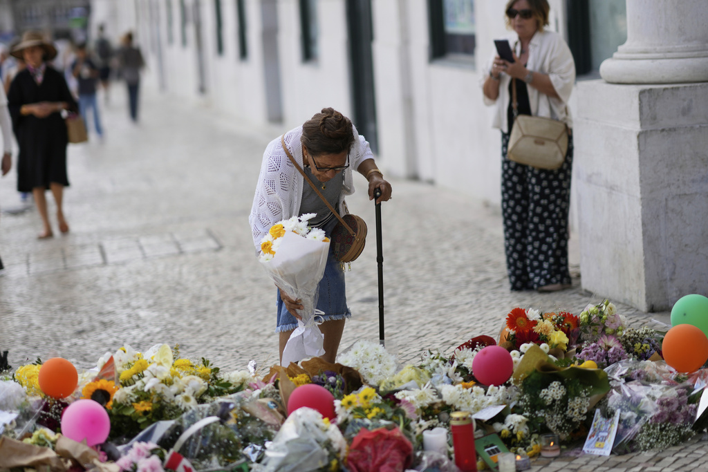 An elderly woman places a bouquet of flowers at a tribute to those that perished in the Gloria funicular, a tourist streetcar that derailed and crashed, in Lisbon, Saturday, Sept. 6, 2025. (AP Photo/Armando Franca)