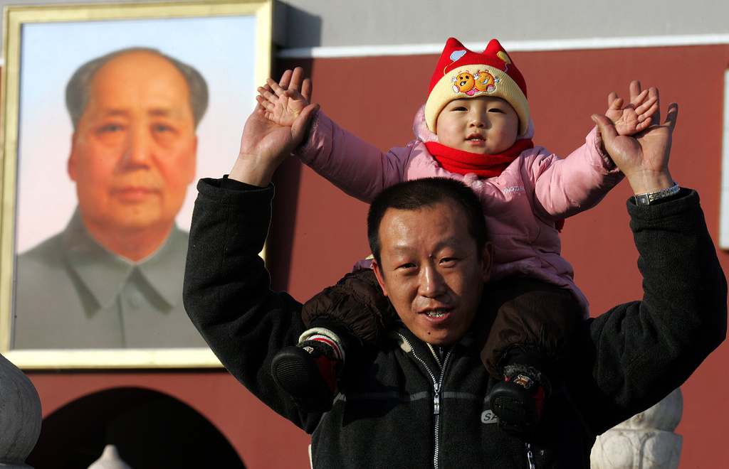 FILE - A Chinese man lifts his child onto his shoulders as they pose for a picture in front of a portrait of late communist leader Mao Zedong in Beijing, China, Jan 6, 2005. (AP Photo/Ng Han Guan, File)