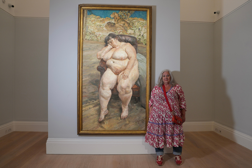 Sue Tilley, a model for British painter Lucian Freud, poses in front of Freud's painting of her, titled "Sleeping by the Lion Carpet" during an interview in Sotheby's auction house in London, Thursday, May 28, 2026. (AP Photo/Kin Cheung)
