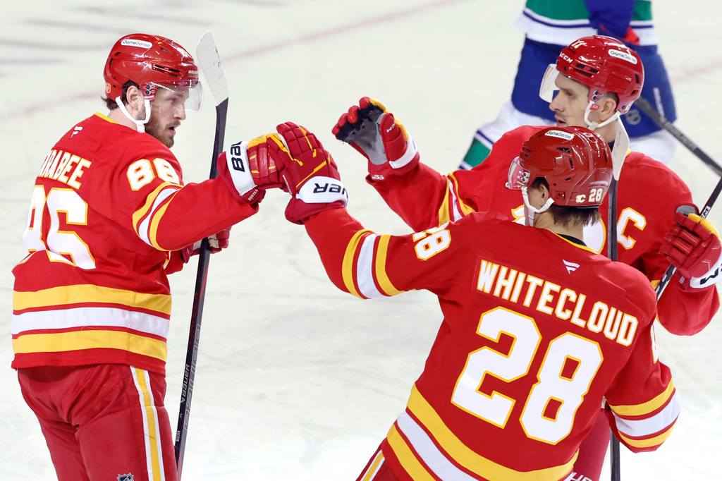 Calgary Flames' Joel Farabee (86) celebrates after his goal against the Vancouver Canucks with teammates Mikael Backlund, back right, and Zach Whitecloud (28) during first-period NHL hockey game action in Calgary, Alberta, Saturday, March 28, 2026. (Larry MacDougal/The Canadian Press via AP)