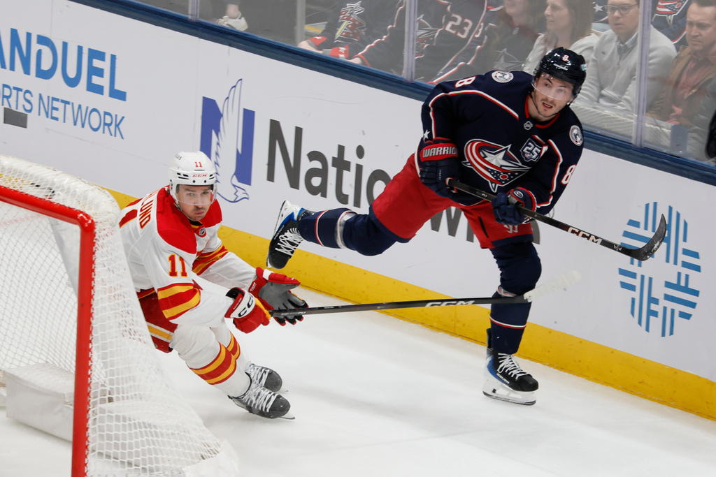 Columbus Blue Jackets' Zach Werenski, right, clears the puck past Calgary Flames' Mikael Backlund during the second period of an NHL hockey game, Tuesday, Jan. 13, 2026, in Columbus, Ohio. (AP Photo/Jay LaPrete)