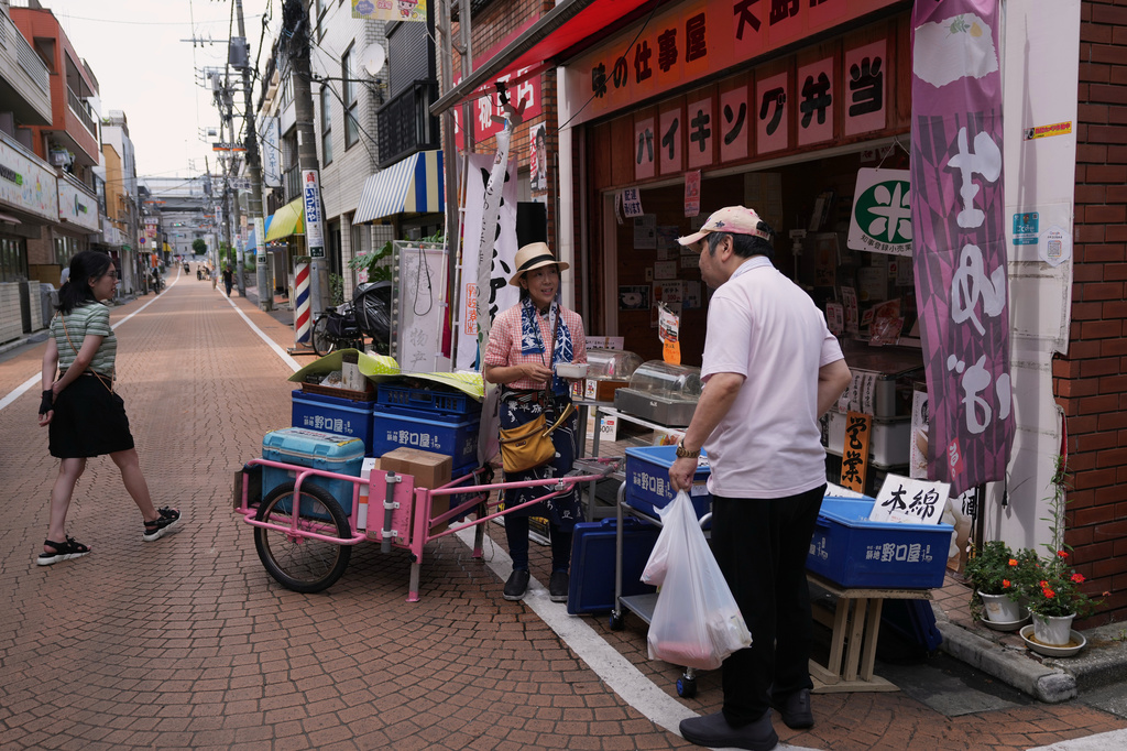Akiko Sugaya helps a customer asking for tofu at her takeout lunch shop, which turns into a dine-in restaurant in the evening, before she starts peddling with her cart in Tokyo, Saturday, July 4, 2026. (AP Photo/Hiro Komae)