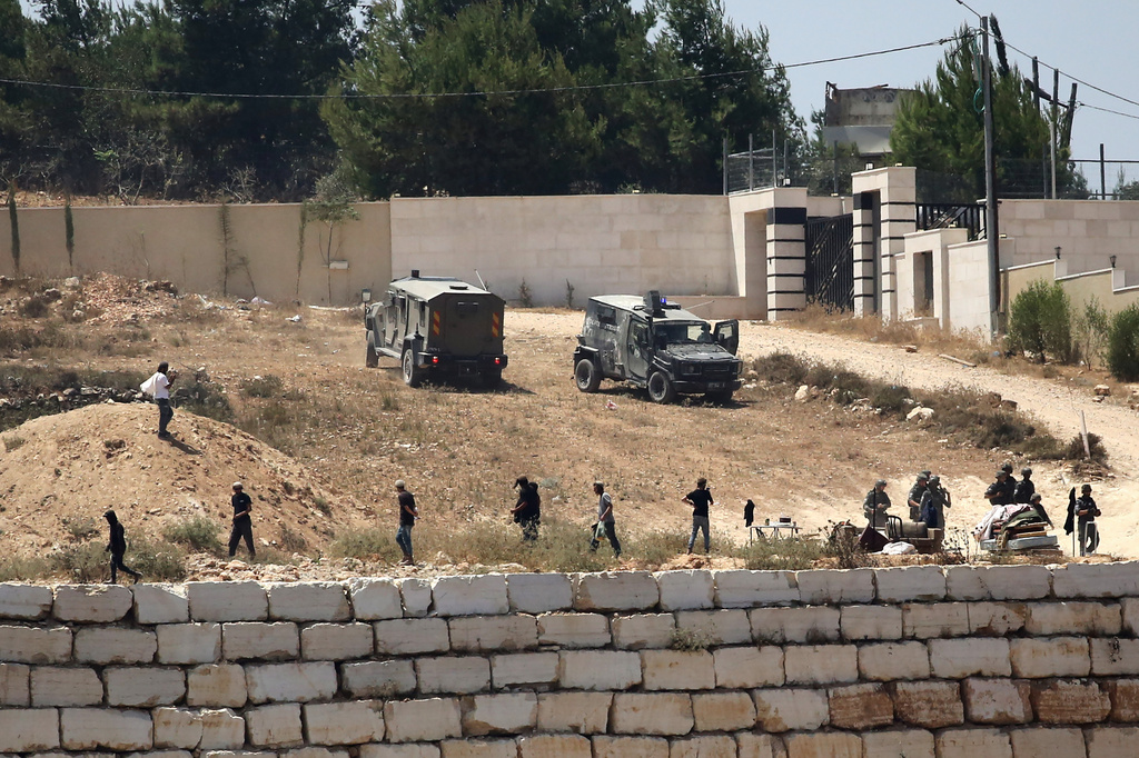 Israeli soldiers stand guard next to settlers in front of Palestinian homes that they have blockaded in the village of Qusra, south of Nablus, in the occupied West Bank, Wednesday, Aug. 12, 2026. (AP Photo/Nidal Eshtayeh)
