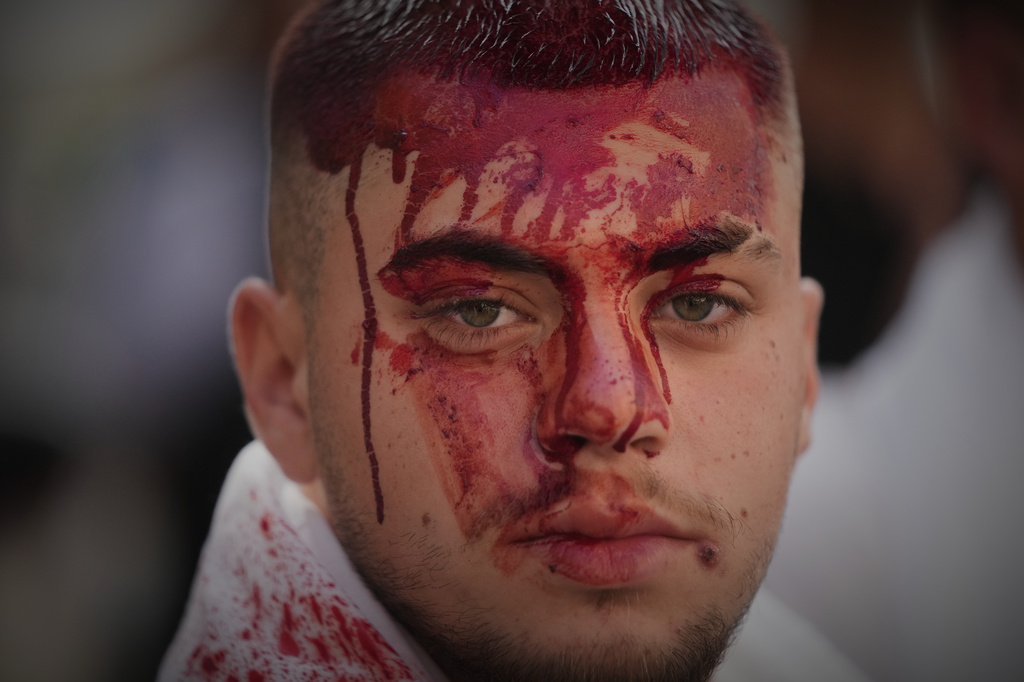 EDS NOTE: GRAPHIC CONTENT - A man bleeds from a ceremonial head wound during Ashoura, when Shiites commemorate the martyrdom of Imam Hussein, the grandson of the Prophet Muhammad, amid buildings destroyed by Israeli strikes in Nabatiyeh, southern Lebanon, Friday, June 26, 2026. (AP Photo/Hassan Ammar)
