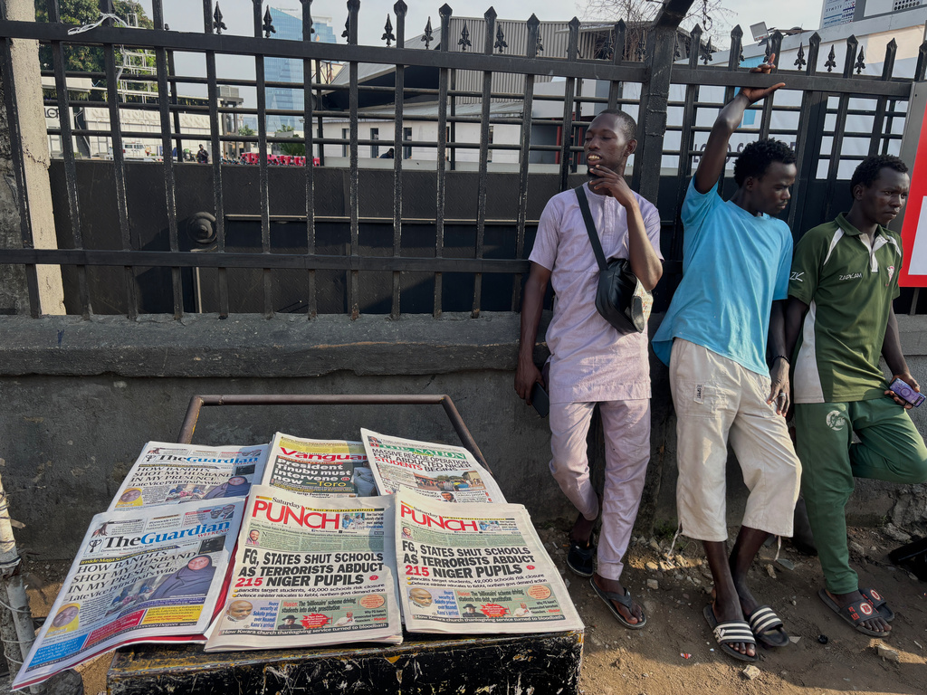 People stand near a display local newspapers on the street of Lagos with headlines on gunmen abducting schoolchildren and staff of the St. Mary's Catholic Primary and Secondary School in Papiri community in Nigeria, Saturday, Nov. 22, 2025. (AP Photo/Sunday Alamba )