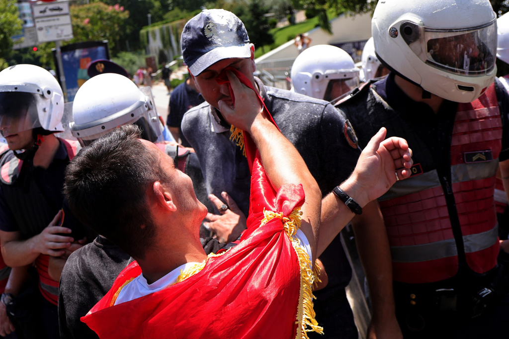 A protester uses a flag to wipe flour from a police officer's face during clashes at an anti-government rally in Tirana, Albania, Thursday, July 2, 2026. (AP Photo/Hameraldi Agolli)