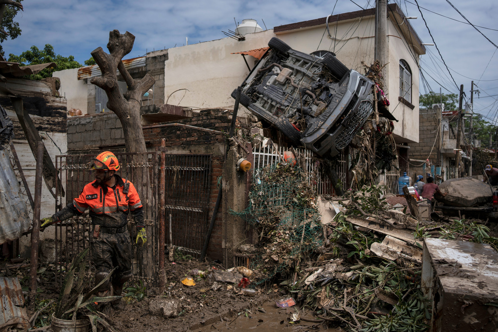 A rescue worker, part of the volunteer brigade known as the Topos, works near a car hanging over a fence by a damaged house in Poza Rica, Mexico, Monday, Oct. 13, 2025, after torrential rains. (AP Photo/Felix Marquez)