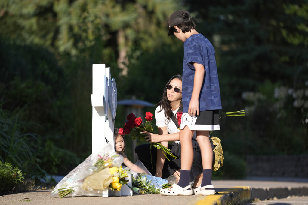 Amy Dols, and her children, Archie and Paloma place flowers at a memorial at Annunciation Catholic Church after Wednesday's school shooting, Thursday, Aug. 28, 2025, in Minneapolis. (AP Photo/Abbie Parr)