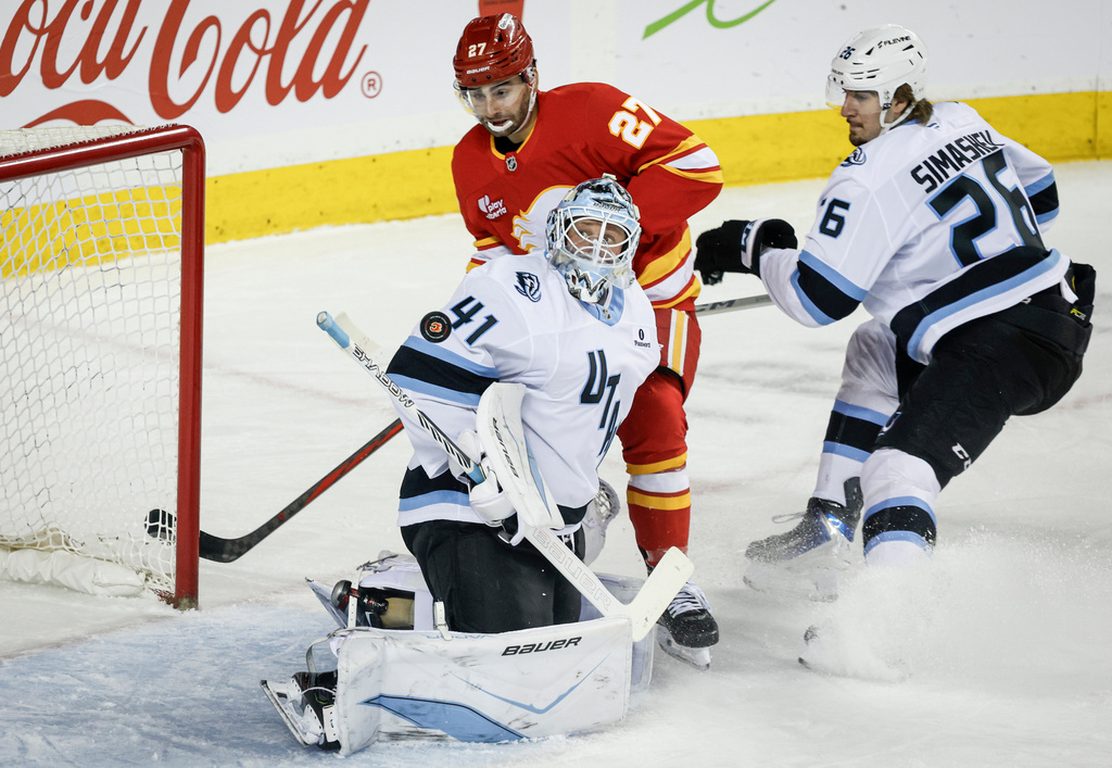 Utah Mammoth goalie Vitek Vanecek, centre, follows the puck as Calgary Flames' Matt Coronato, left, and Dmitri Simashev look on during first period NHL hockey action in Calgary, Alberta, Sunday, April 12, 2026. (Jeff McIntosh/The Canadian Press via AP)