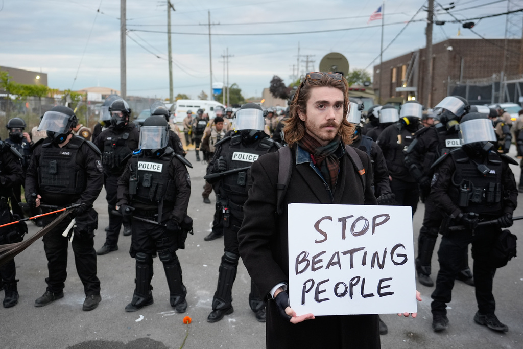 A demonstrator holds a sign reading "STOP BEATING PEOPLE" near a line of law enforcement as protesters gather outside an ICE processing facility in the Chicago suburb of Broadview, Ill., Saturday, Nov. 1, 2025. (AP Photo/Alex Brandon)