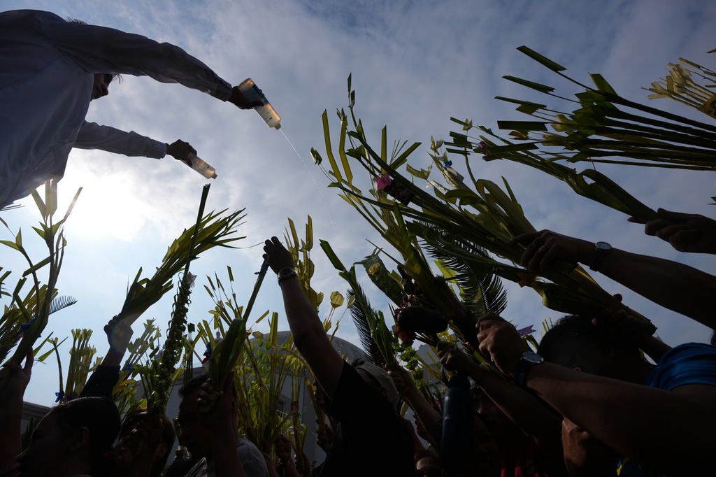 A church worker uses two bottles to sprinkle holy water on the palm fronds of devotees during blessing rites outside the Antipolo Cathedral in Antipolo city, Rizal province Philippines as they observe Palm Sunday, March 29, 2026. (AP Photo/Aaron Favila)