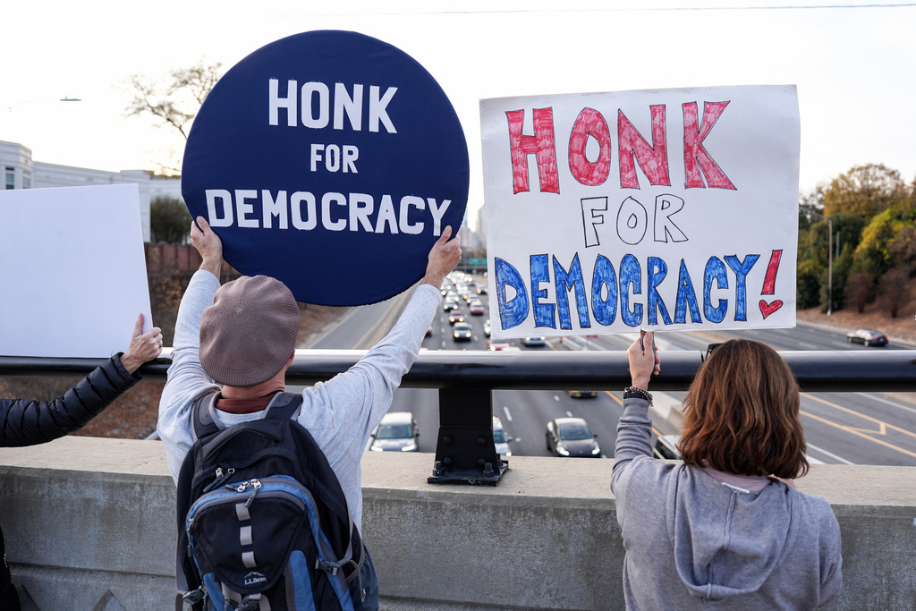 Protesters hold signs amid the arrival of federal law enforcement, Tuesday, Nov. 18, 2025, in Charlotte, N.C. (AP Photo/Matt Kelley)