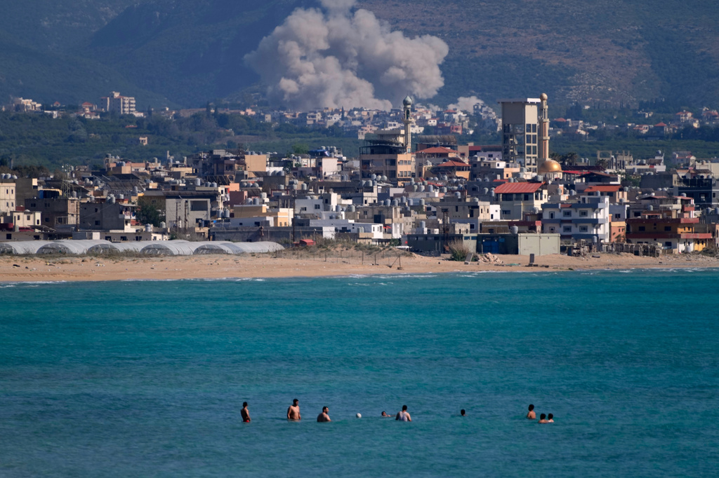 People swim on a public beach as smoke, background, rises from an Israeli airstrike that hit the Qlaileh village, seen from the southern port city of Tyre, Lebanon, Tuesday, June 2, 2026. (AP Photo/Mohammed Zaatari)