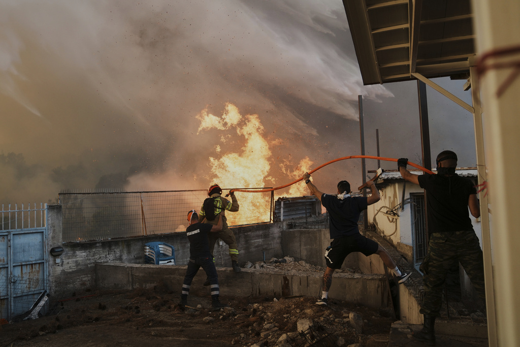 A firefighter and men try to control the fire approaching a house during a wildfire in Patras city, western Greece, Wednesday, Aug. 13, 2025. (AP Photo/Thanassis Stavrakis)