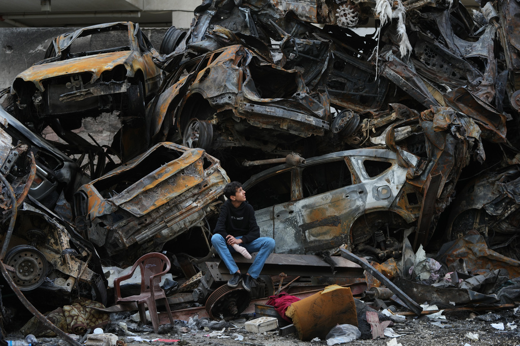 A man sits next to charred cars and wreckage where a building was destroyed by an Israeli airstrike the previous Wednesday, in central Beirut, Lebanon, Tuesday, April 14, 2026. (AP Photo/Hassan Ammar)