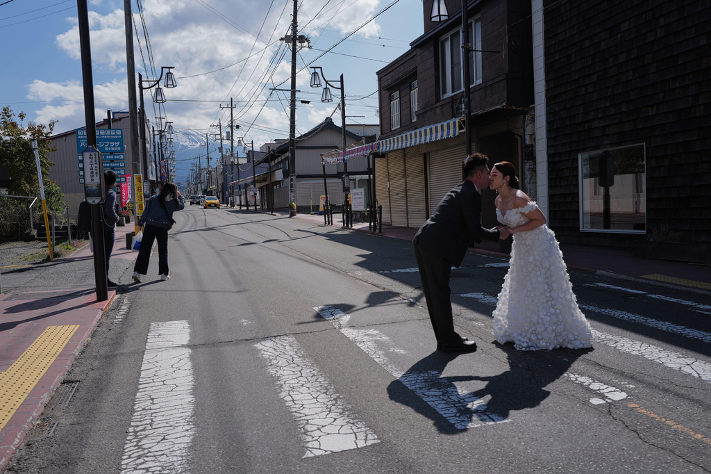Foreign visitors pose for photos at Honcho Street with Mt. Fuji as background on Wednesday, April 8, 2026, in Fujiyoshida, west of Tokyo. (AP Photo/Eugene Hoshiko)