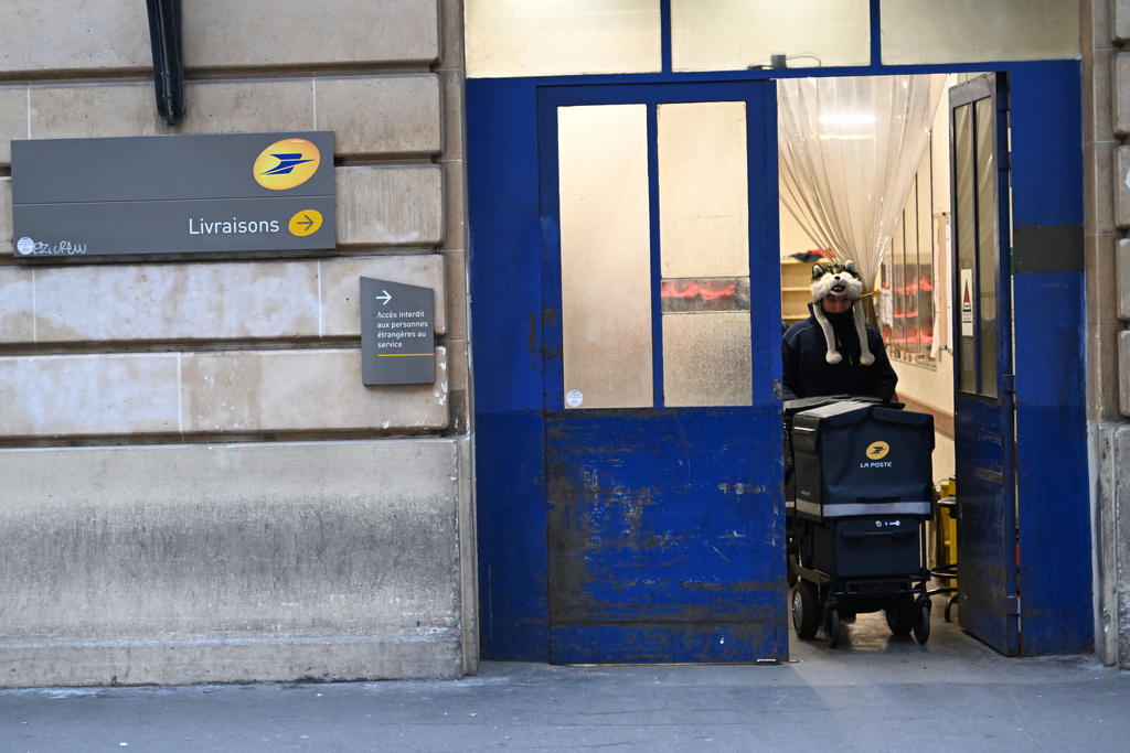 A postal delivery man leaves a post office, Tuesday, Dec. 23, 2025 in Paris. (AP Photo/Emma Da Silva)