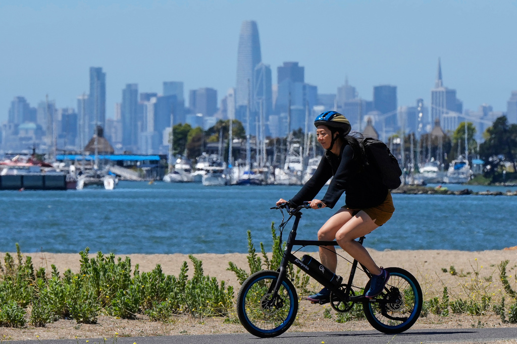 FILE - A woman rides a bicycle on a path, as the San Francisco skyline is seen in the background, Aug. 19, 2025, in Alameda, Calif. (AP Photo/Godofredo A. Vásquez, File)
