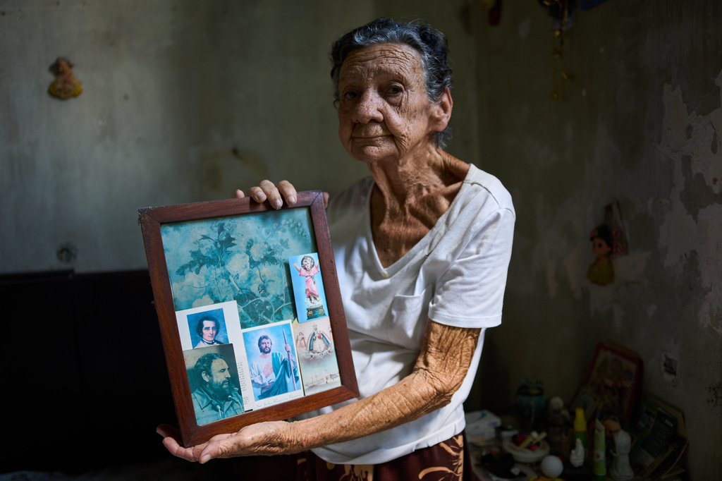 Mercedes Lopez Rey holds a framed cyanotype with an image of the late Cuban President Fidel Castro and prayer cards tucked into the edges of the frame, in her home in Old Havana, Cuba, Friday, April 10, 2026. (AP Photo/Ramon Espinosa)