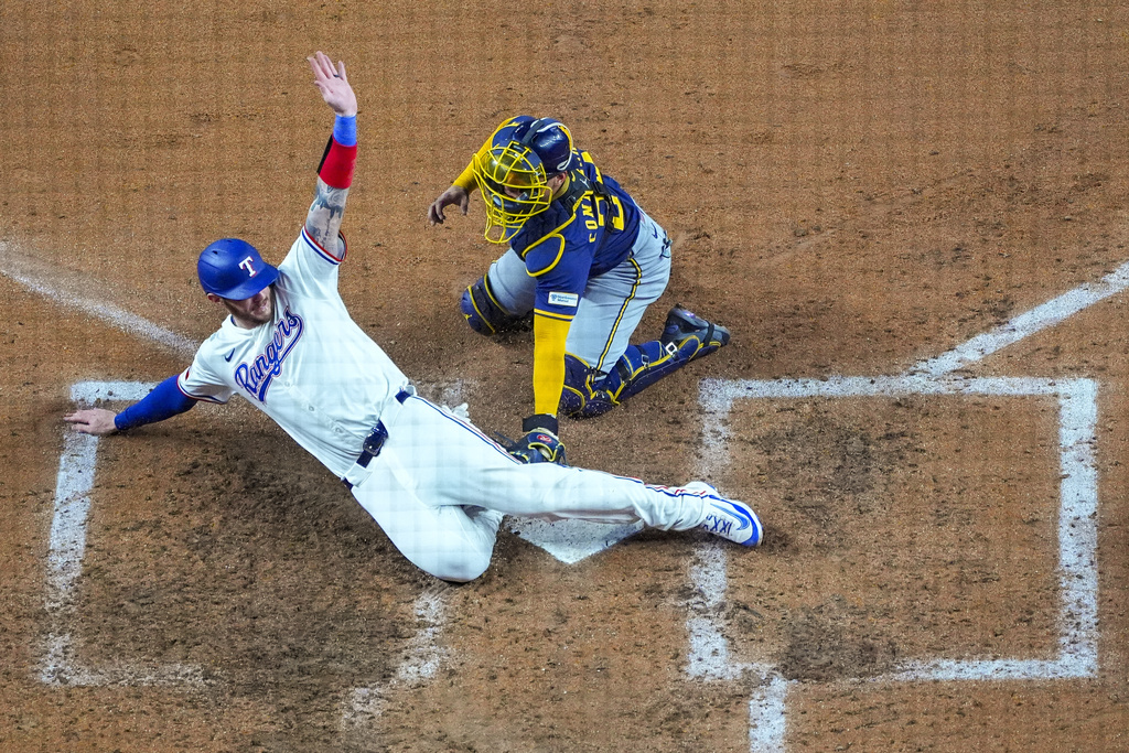 Texas Rangers' Jonah Heim, bottom, slides in to score ahead of the tag of Milwaukee Brewers catcher William Contreras on a double by Rangers' Michael Helman during the seventh inning of a baseball game Monday, Sept. 8, 2025, in Arlington, Texas. (AP Photo/Julio Cortez)