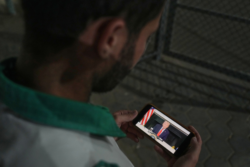 Palestinian paramedic Saeed Awad looks at his phone displaying an image of U.S. President Donald Trump, following the announcement that Israel and Hamas have agreed to the first phase of a peace plan to pause fighting, as he stands at Al-Aqsa Hospital, in Deir al-Balah, in the central Gaza Strip, Thursday, Oct. 9, 2025. (AP Photo/Abdel Kareem Hana)