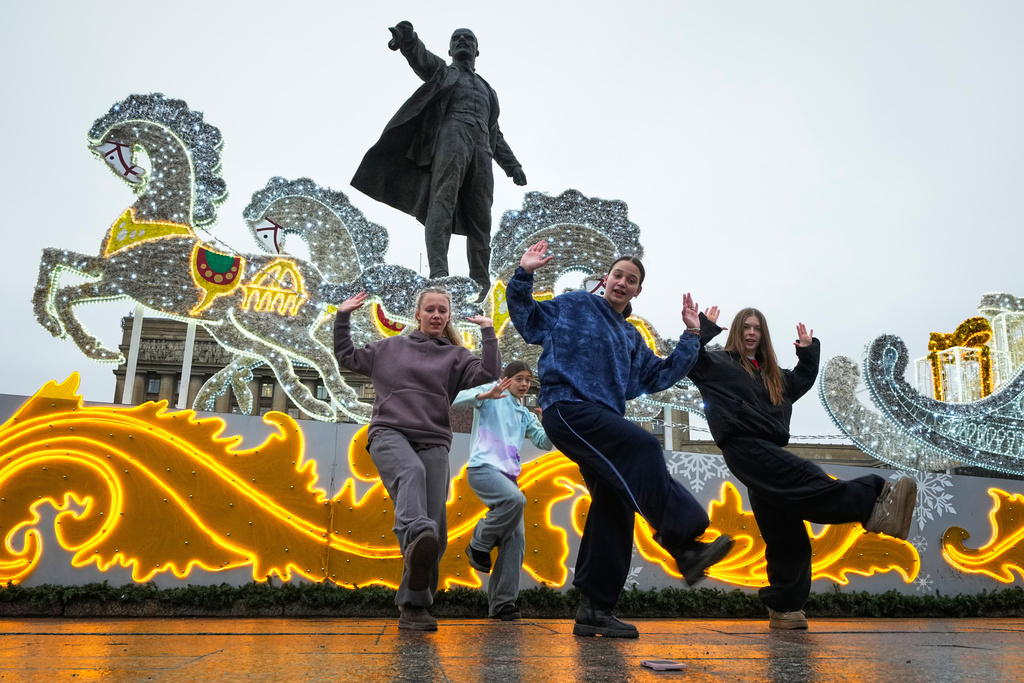 Girls film their dance at a Christmas fair opened prior to Christmas and New Year festivities in St. Petersburg, Russia, Thursday, Dec. 25, 2025, with a statue of Soviet Union founder Vladimir Lenin in the background. (AP Photo/Dmitri Lovetsky)