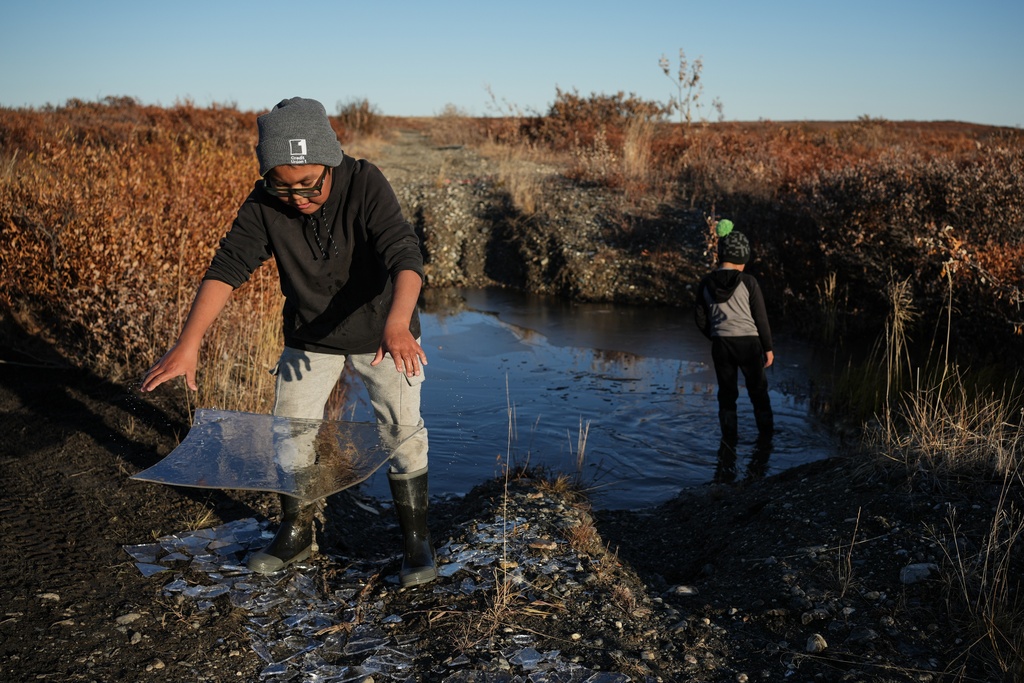 Charles Gallahorn, 10, plays with a slab of ice taken from a pond that formed on a warped road caused by thawing permafrost in Kotzebue, Alaska, Friday, Sept. 26, 2025. (AP Photo/Annika Hammerschlag)
