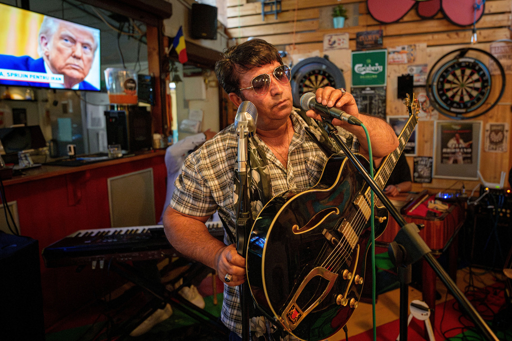FILE - Tudor Lakatos, who goes by the stage name Elvis Rromano, tests the microphone at the Terasa Florilor restaurant before performing as President Donald Trump appears on a television screen during a news broadcast, in Bucharest, Romania, June 20, 2025. (AP Photo/Andreea Alexandru, File)