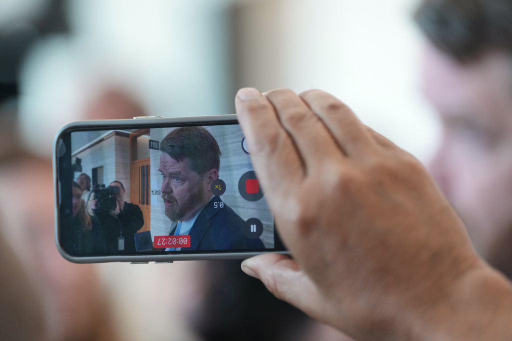 A person records with a smartphone Mark Bankston, an attorney for relatives of the victims of the 2012 Sandy Hook School shooting, as he speaks to the media following a hearing at the county courthouse in Austin, Texas, Thursday, April 30, 2026. (AP Photo/Eric Gay)