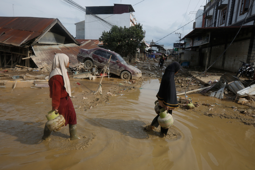 FILE - Survivors walk past the wreckage of a car at an area affected by flash flooding in the aftermath of Cyclone Senyar in Aceh Tamiang, on Sumatra Island, Indonesia, Thursday, Dec. 4, 2025. (AP Photo/Binsar Bakkara, File)