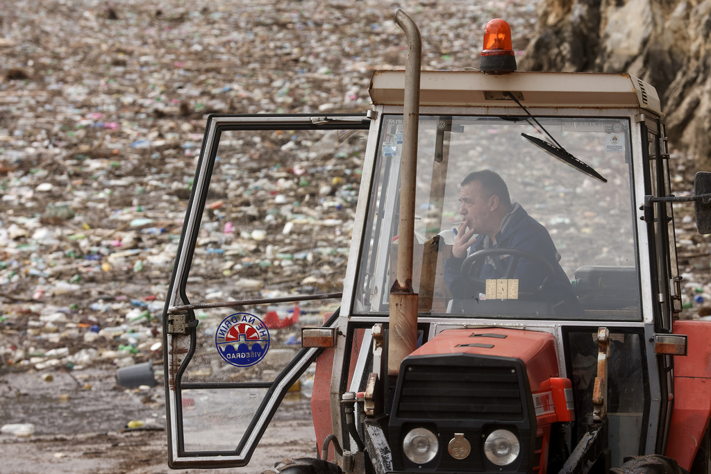 A worker takes a break, backdropped by tons of waste floating as it clogs the Drina river in Visegrad, Bosnia, Thursday, Feb. 5, 2026. (AP Photo/Armin Durgut)