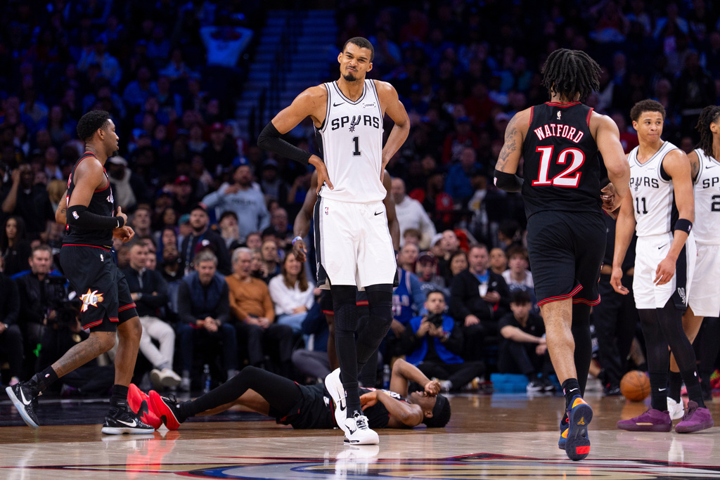 San Antonio Spurs' Victor Wembanyama, center, reacts to the foul by Carter Bryant, right, on Philadelphia 76ers' VJ Edgecombe, center floor, during the first half of an NBA basketball game, Tuesday, March 3, 2026, in Philadelphia. (AP Photo/Chris Szagola)