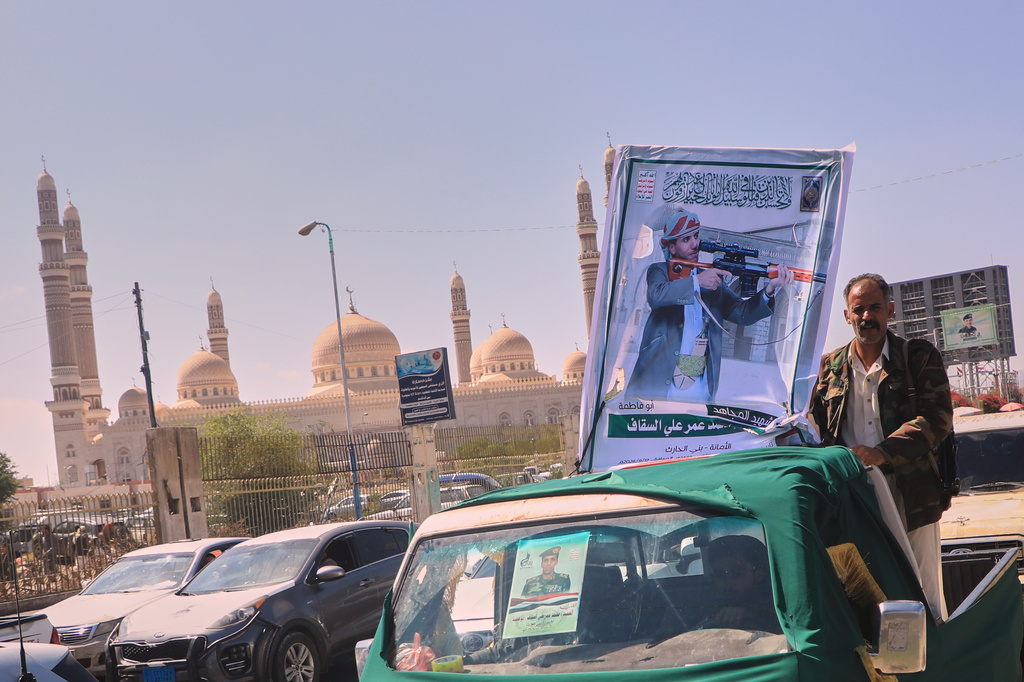 A man stands beside a portrait of Houthi fighter Mohammed Omar Ali al-Saqqaf, also known as Abu Fatima, mounted on a pickup truck during a mass funeral procession, with Al-Saleh Mosque in the background, in Sanaa, Yemen, Wednesday, Sept. 16, 2026. (AP Photo)
