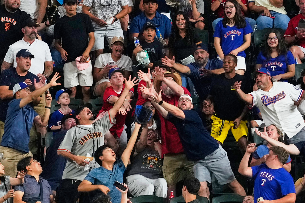 Fans compete for a San Francisco Giants' Jung Hoo Lee home run ball in the third inning of a baseball game against the Texas Rangers in Arlington, Texas, Monday, Aug. 3, 2026. (AP Photo/Tony Gutierrez)