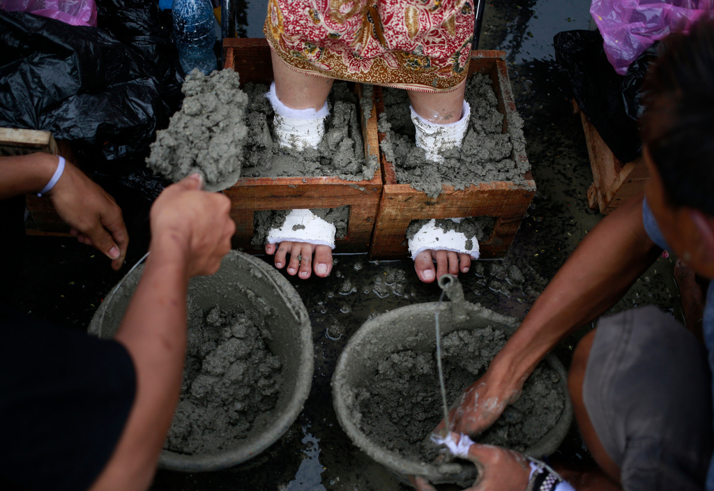 FILE - An activist has her feet cemented in a wooden case during a rally against the operation of a cement factory in Kendeng Mountains, Central Java, outside the presidential palace in Jakarta, Indonesia on Monday, March 20, 2017.(AP Photo/Dita Alangkara, File)