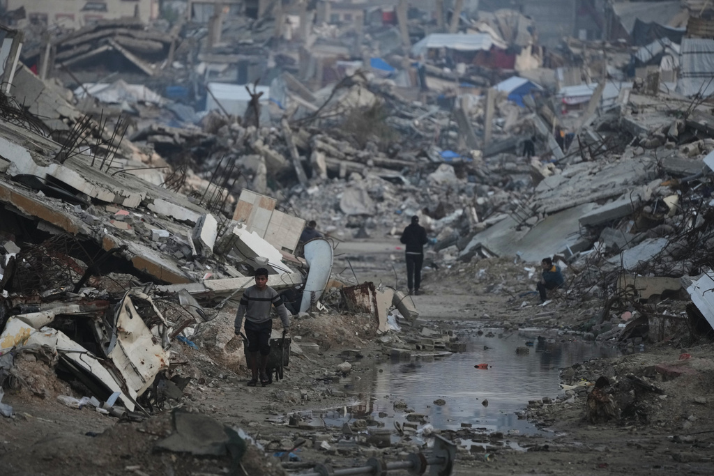 Palestinians walk amid buildings destroyed by Israeli air and ground operations in Gaza City, Tuesday, Jan. 6, 2026. (AP Photo/Jehad Alshrafi)