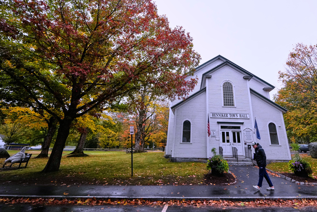 A student walks past trees with colorful fall foliage, Tuesday, Oct. 14, 2025, in Henniker, N.H. (AP Photo/Charles Krupa)