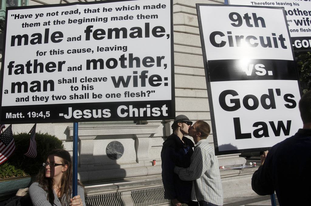 FILE - Aiden Lougee, center left, kisses his boyfriend, Rex Resa, seen between signs held by opponents to gay marriage outside of the courthouse after a hearing in the Ninth Circuit Court of Appeals, Monday, Dec. 6, 2010, in San Francisco. (AP Photo/Jeff Chiu, File)