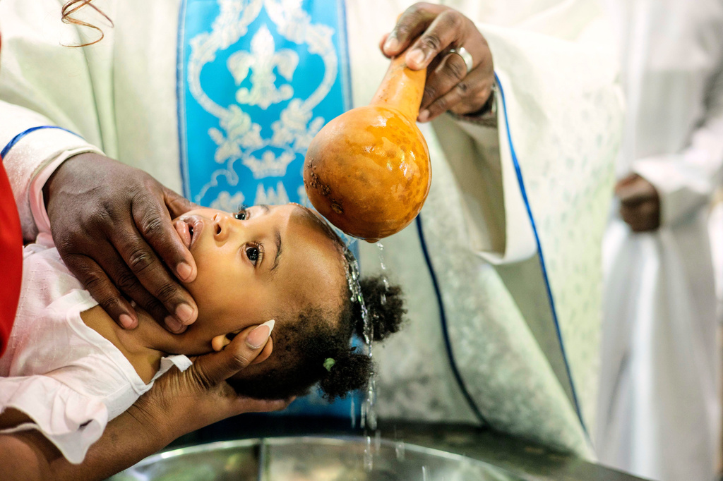 A priest pours water over the head of a child during a baptism ceremony at the Roman Catholic Cathedral in Harare, Zimbabwe, Sunday, April 5, 2026. (AP Photo/Aaron Ufumeli)