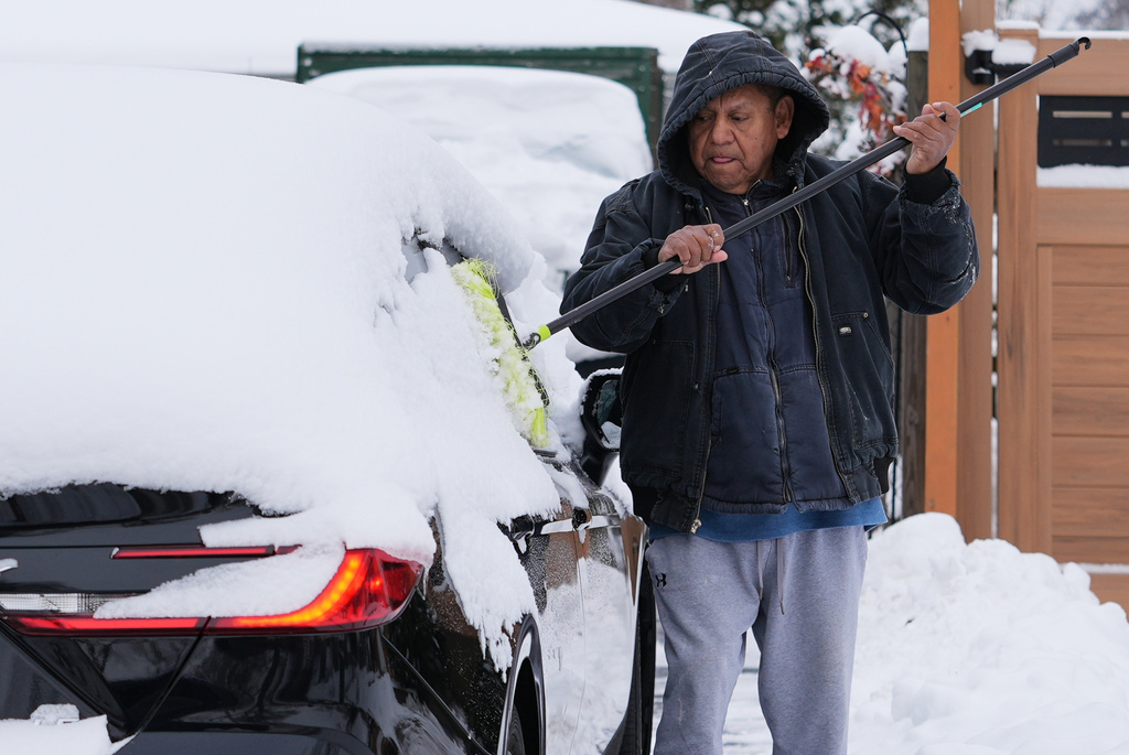A person cleans the snow off of a car during a cold day in Wheeling, Ill., Tuesday, Dec. 2, 2025. (AP Photo/Nam Y. Huh)