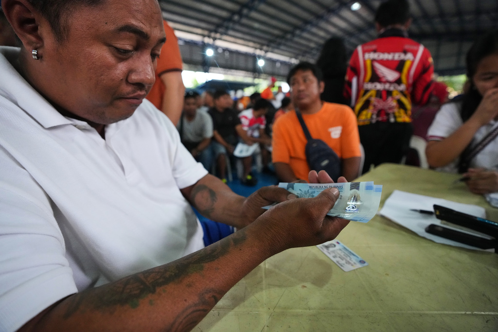 A tricycle driver receives cash assistance from the government to help their livelihood as oil prices continue to rise on Tuesday, March 17, 2026, in Manila, Philippines. (AP Photo/Aaron Favila)