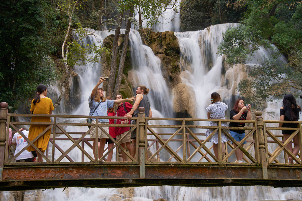 Tourists pose for photos on a footbridge in front of Kuang Si Waterfall near Luang Prabang, Laos, one of the country's most popular natural attractions known for its multi-tiered limestone cascades and turquoise pools on Tuesday, Nov. 4, 2025. (AP Photo/Eugene Hoshiko)