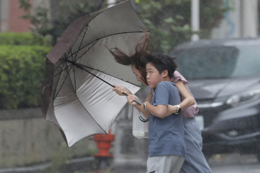People struggle with umbrella in a rain caused by Typhoon Bavi in Taichung, Taiwan, Saturday, July 11, 2026. (AP Photo/Chiang Ying-ying)
