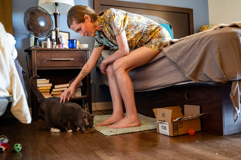 Mari Younger pets her cat Stella inside her converted hotel room where she lives after being displaced two years prior by the Maui fires, in Kihei, Hawaii, Wednesday, March 4, 2026. (AP Photo/Mengshin Lin)