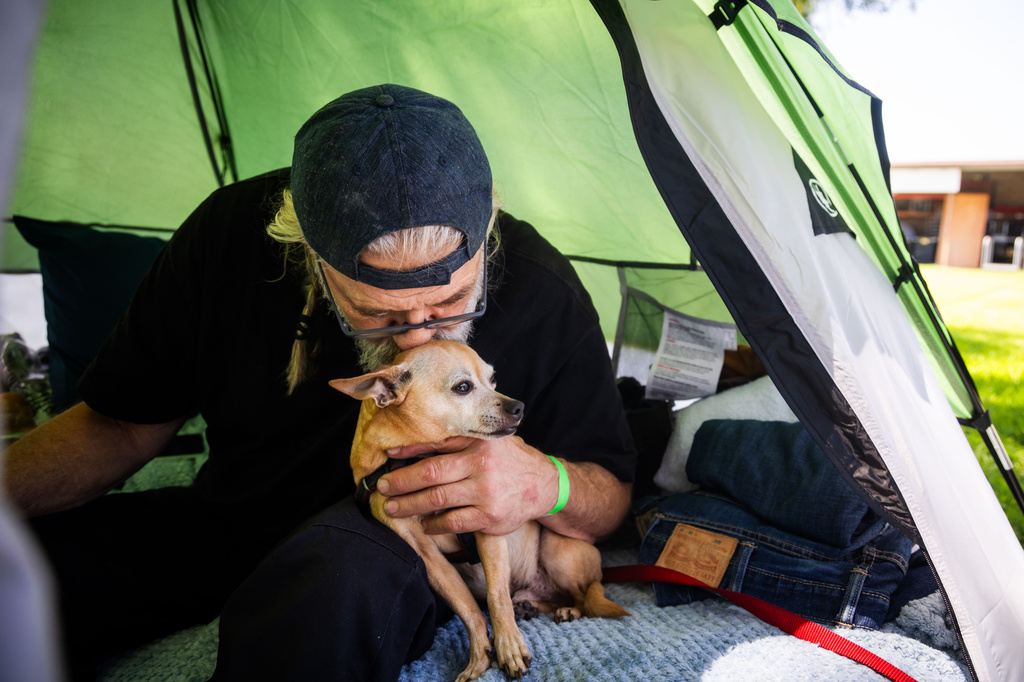 Jan De Jonge kisses a pet while sitting inside a tent with their belonging outside the Elks Lodge in Garden Grove, Calif., on Monday, May 25, 2026. (AP Photo/Ethan Swope)