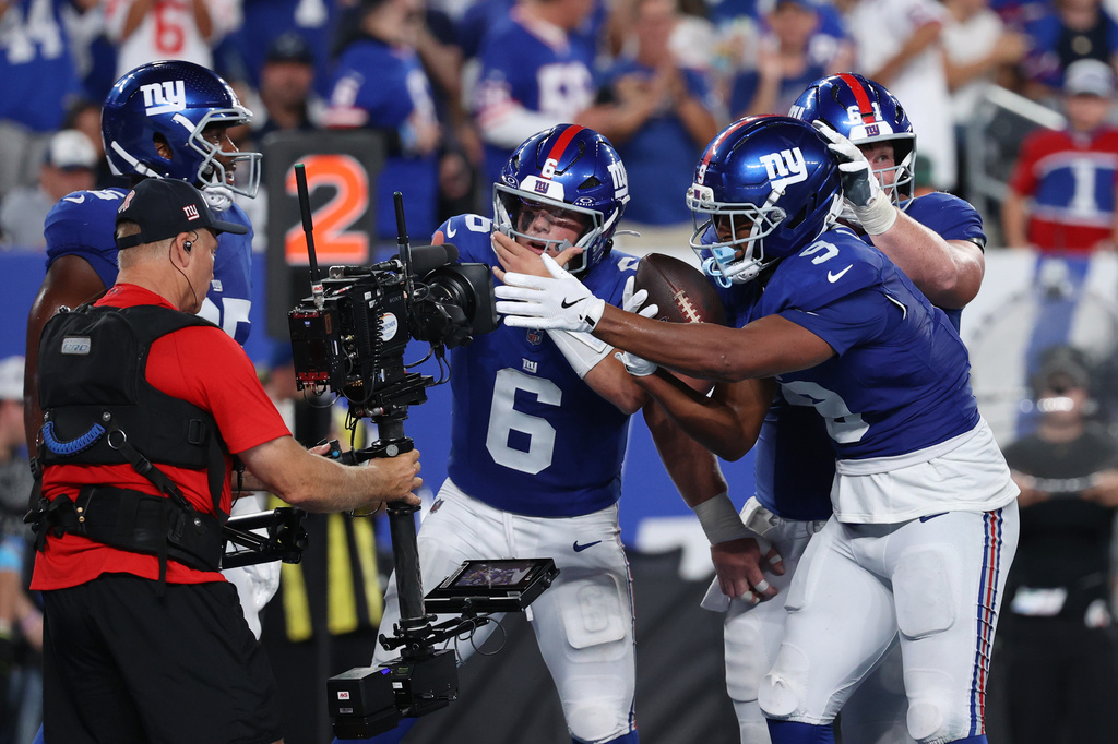 New York Giants quarterback Jaxson Dart (6), tight end Isaiah Likely (9) and center John Michael Schmitz, back right, react in front of a television camera after Likely caught a touchdown pass from Dart against the Dallas Cowboys during the second half of an NFL football game Sunday, Sept. 13, 2026, in East Rutherford, N.J. (AP Photo/Pamela Smith)