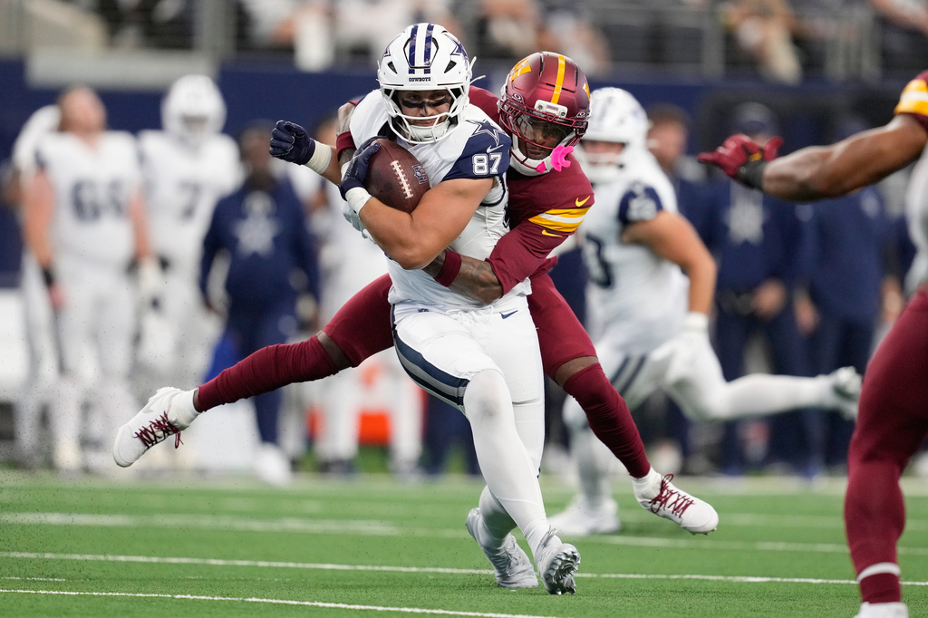 Dallas Cowboys tight end Jake Ferguson (87) runs with the ball as Washington Commanders cornerback Trey Amos during the first half of an NFL football game Sunday, Oct. 19, 2025, in Arlington, Texas. (AP Photo/Tony Gutierrez)